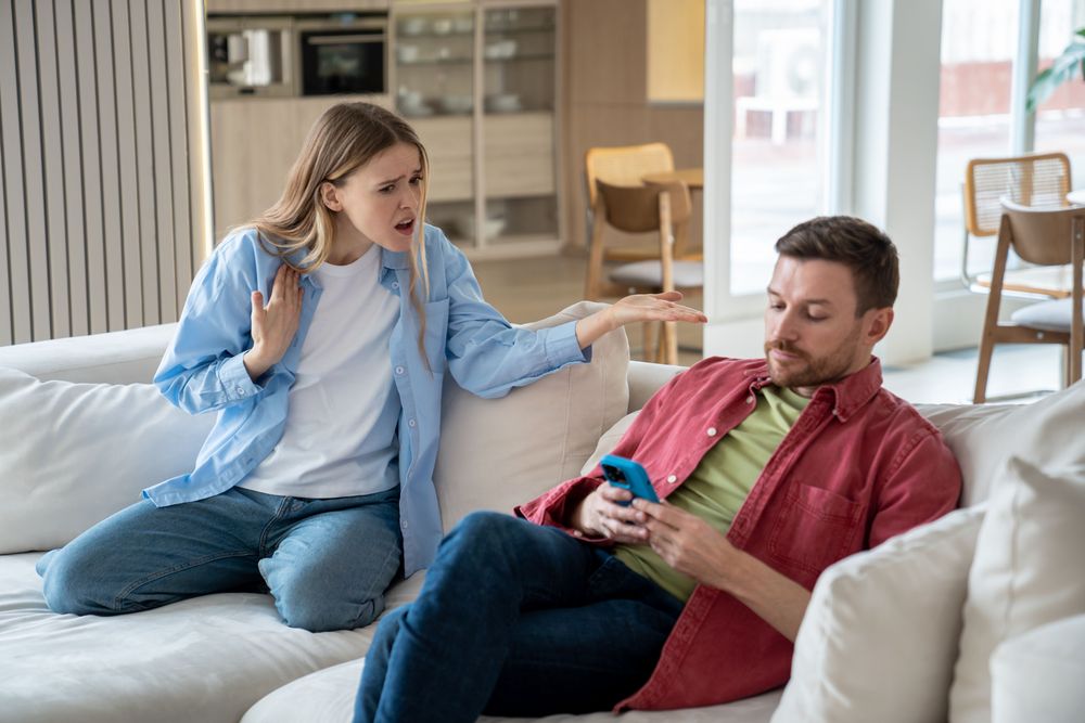 A woman tries to engage a man in conversation, but he ignores her, choosing to pay attention to his phone.