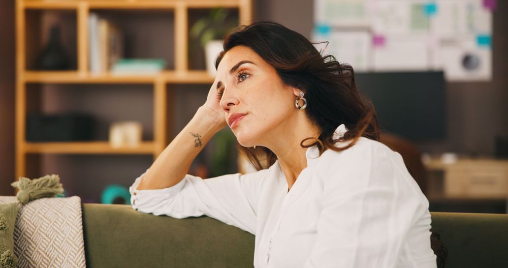 A brown-haired woman sitting on a green couch, looking up in thought