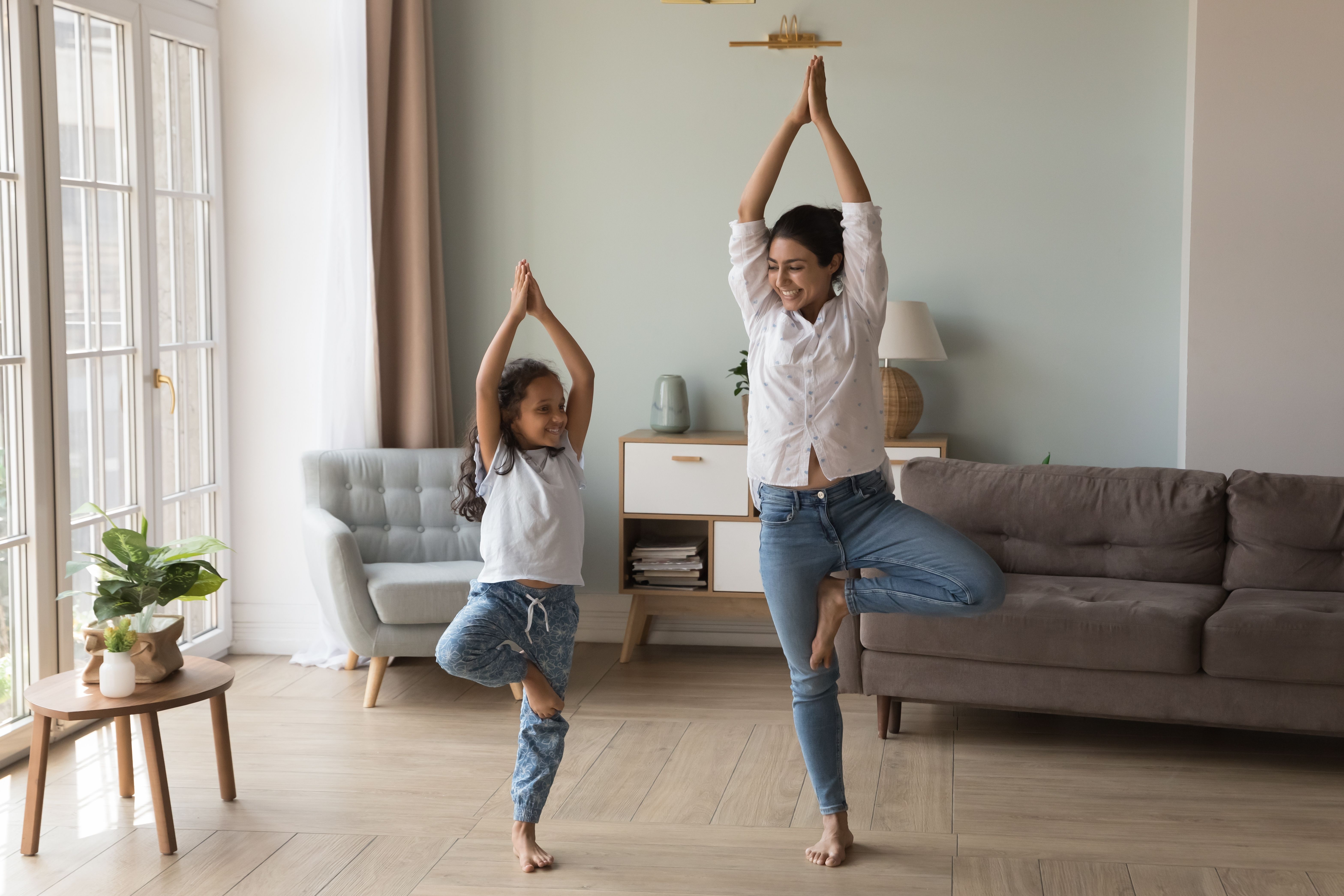 A woman and a child stand together in a room doing yoga together